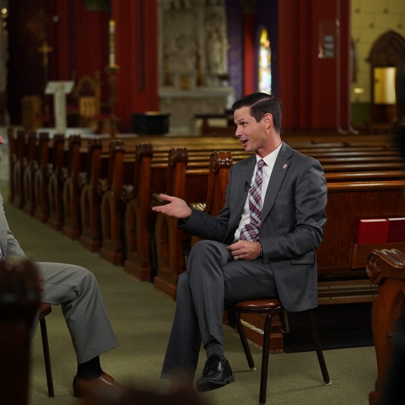 Adam Minihan interviewing a co-host during a podcast recording session inside a church setting